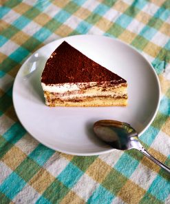 A tempting slice of tiramisu on a white plate with a silver spoon, perfect for dessert lovers.
