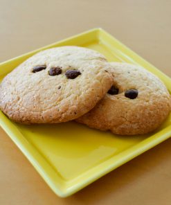 Two freshly baked chocolate chip cookies served on a yellow plate.